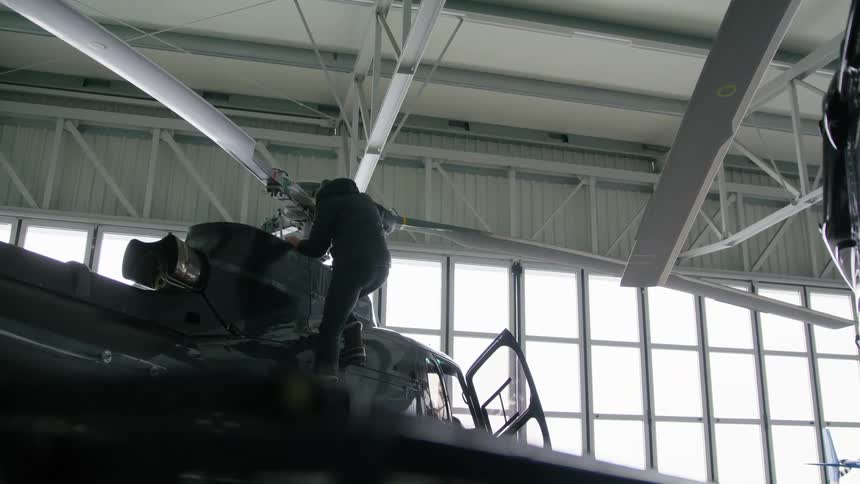A man looks at rotors on a helicopter and then climbs down