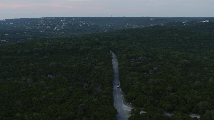 Cars drive by on a long highway surrounded by a forest