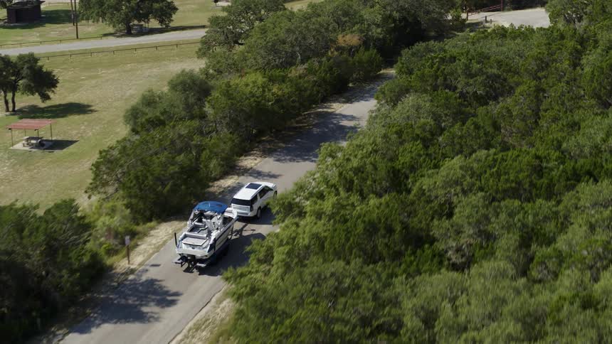 Aerial view of a car towing a boat on a rural road through the countryside