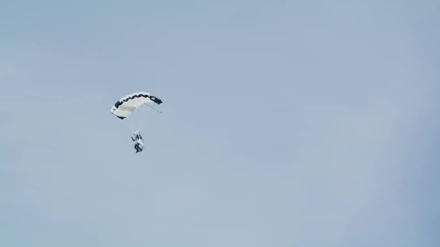 A parachutist gliding on a white parachute on the blue sky at daytime