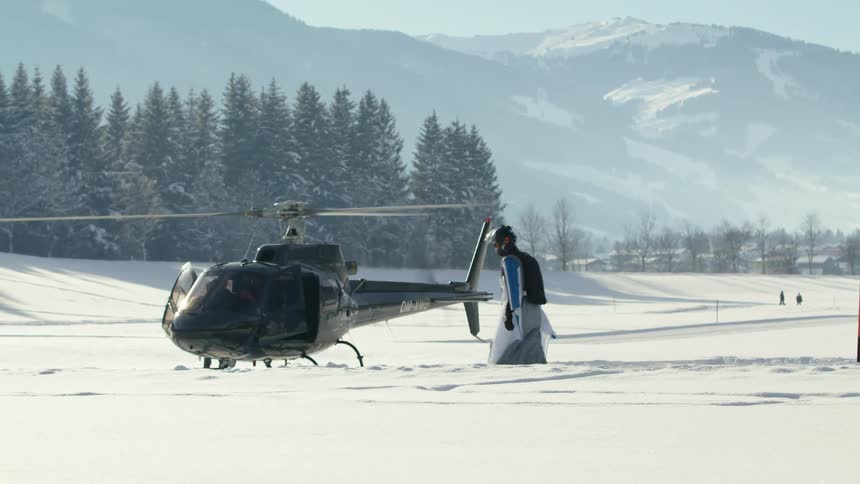 A man walks across a snowy field towards a helicopter