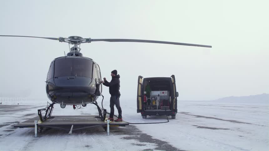 Pilot closes the door of a helicopter parked on a mobile helipad in the snow covered plains next to a van