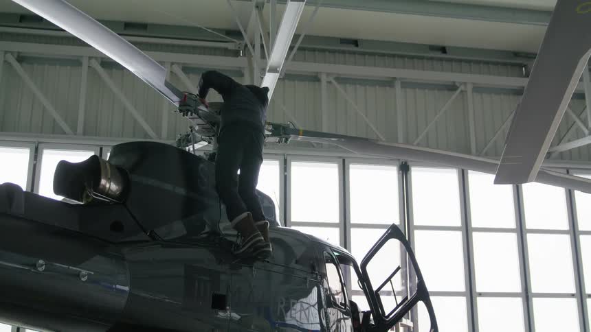 Man checking the rotors of a helicopter parked inside a hangar