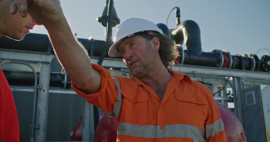 A worker points out things in the surroundings while speaking to a coworker outdoors during the day