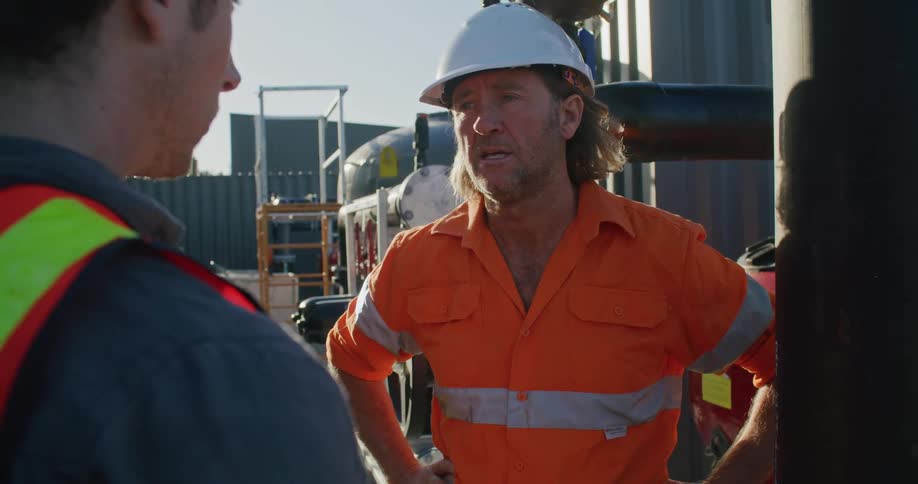 Two coworkers having a conversation outdoors at a processing plant during the day
