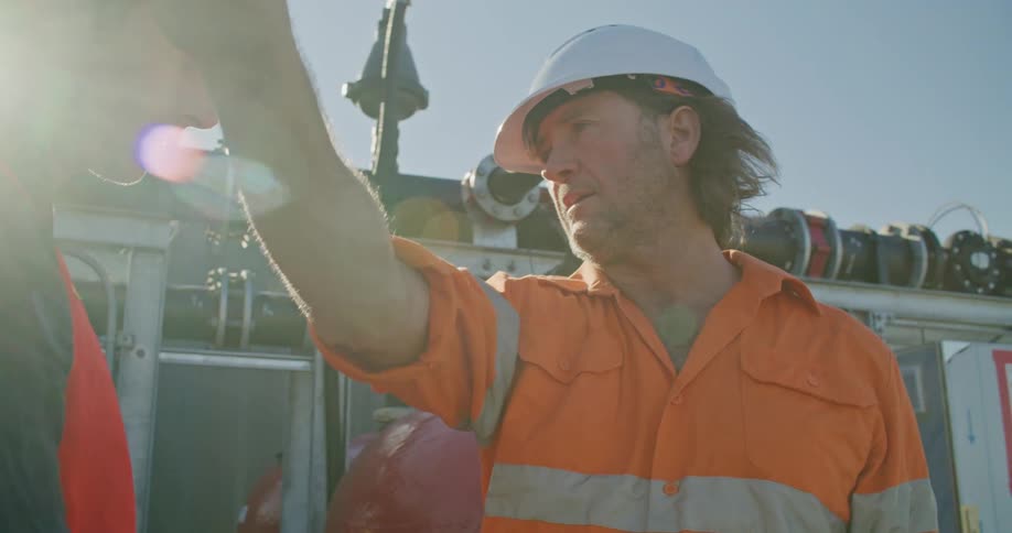 A man in a hard hat gives instructions to another man with a safety vest on