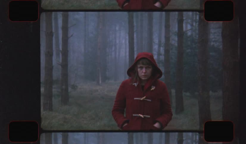 A young woman standing in a foggy forest with her hands in her pockets staring at the camera