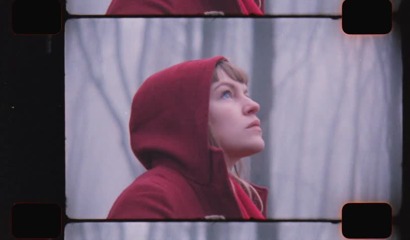 A woman in a forest with a red hoodie with trees the sky and clouds in the background on analog Film 16mm