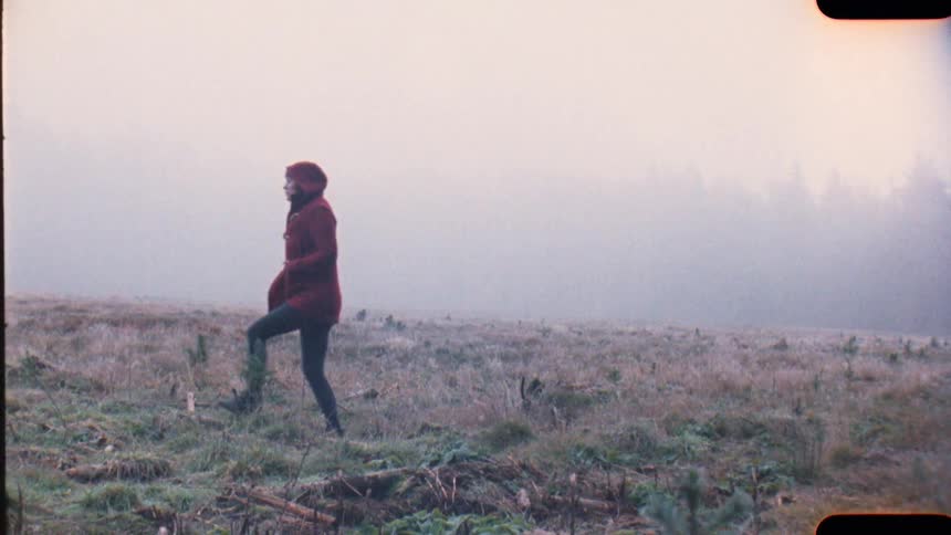 A woman in a rain coat walks past a dense forest on a very foggy day on analog Film 16mm