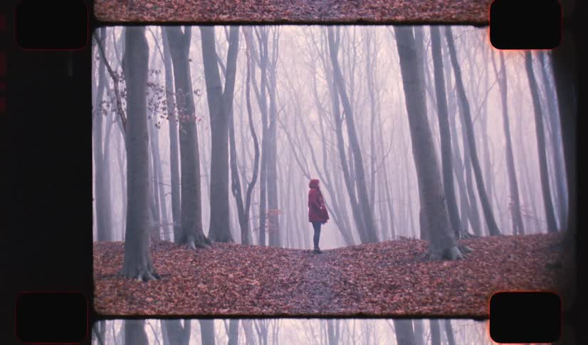 A young woman walking down a path in a misty forest stops to look around at her surroundings on analog Film