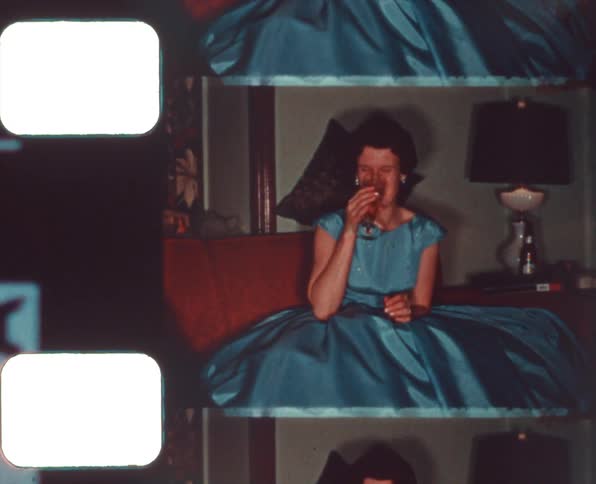 Vintage film footage of a woman sitting on a couch at home drinking wine