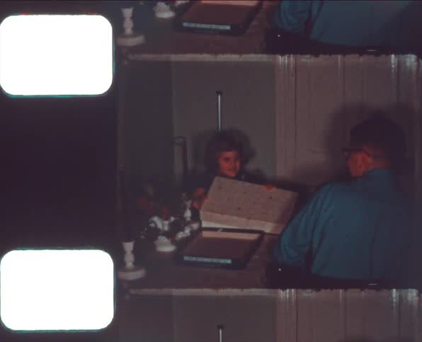 A young girl opens a present as her father watches from across the table