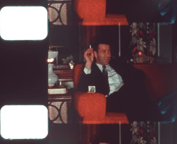 A man in a room sitting on a couch holding a cigarette