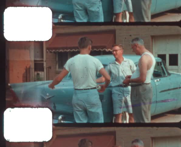A family of men stand near a car in the driveway talking and smiling