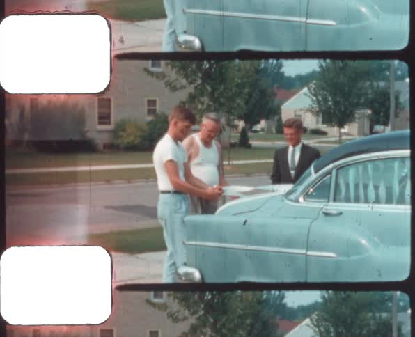 A man decorates a car in a driveway with white ribbon as his dad looks on