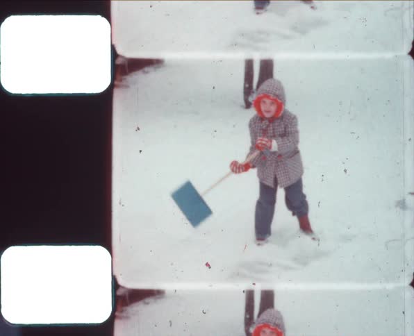 A young child in a hooded winter coat uses a snow shovel to scoop snow off of the ground