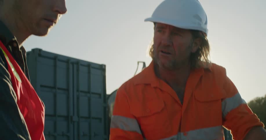 Two construction workers talk and look at a laptop