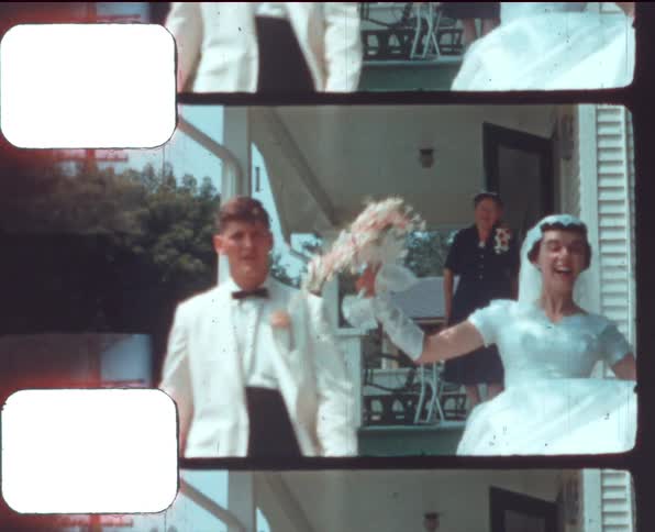 A bride and groom walk down the steps of the side of a house then smile towards the camera