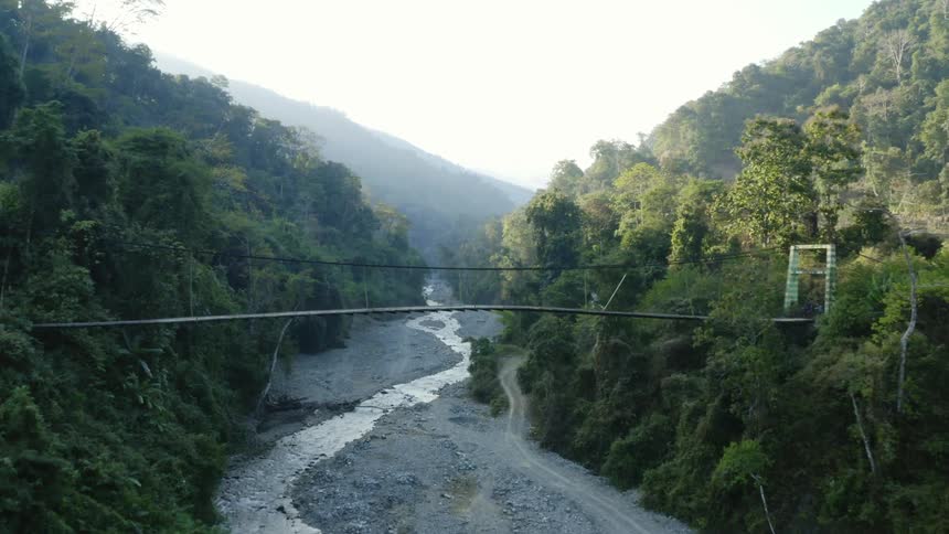 Man runs across cable bridge over winding river between two forest covered mountains