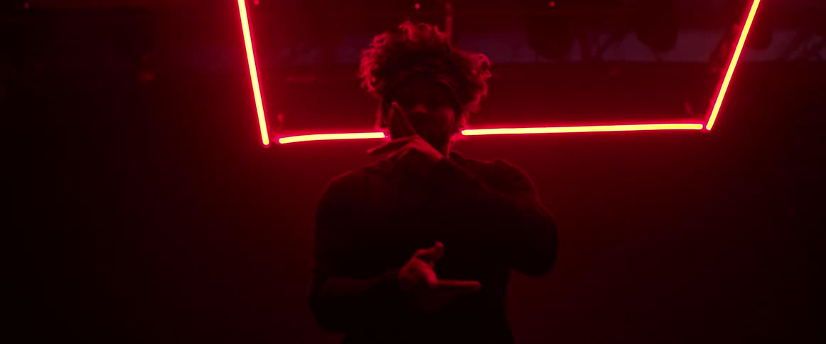 Man wearing a head band dancing on a dark room under red neon lights
