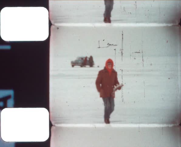 A person with a red hoodie and boots walking on snow and ice holding a fish