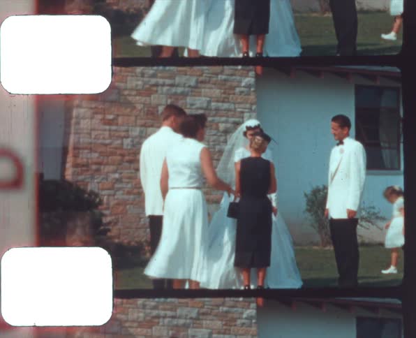 A woman in a white dress walks up and pushes a woman in a black dress as a woman in a wedding dress and two men in white tuxedos laugh