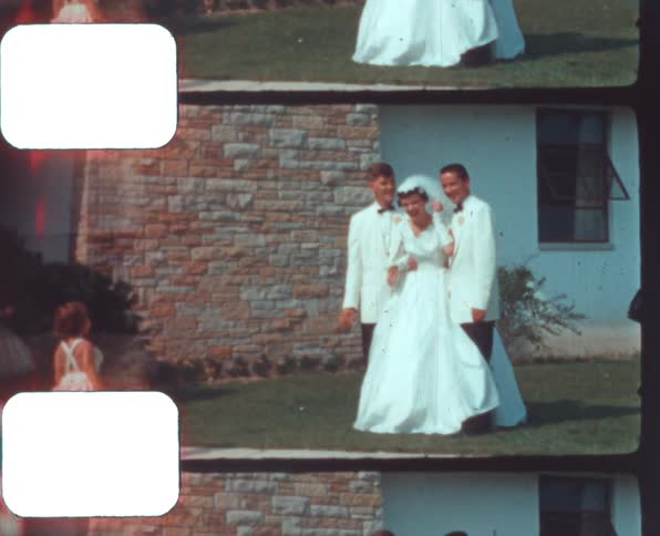 Two young males stand with a woman in her bridal gown as they pose for a photo