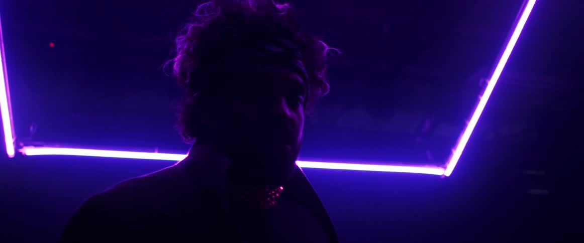 A black male standing in a dark room with neon lighting