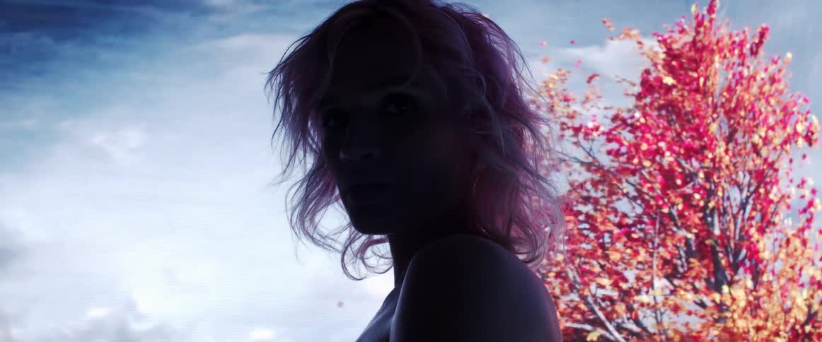 Young woman with pink hair looking at the camera on a dark room in front of a digital display