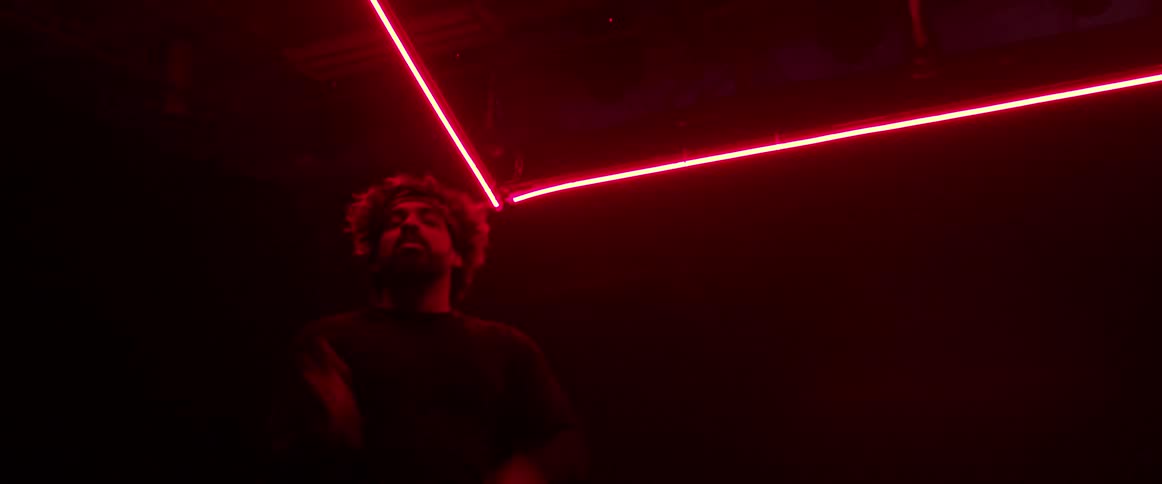 Man wearing a head band dancing on a dark room under red neon lights