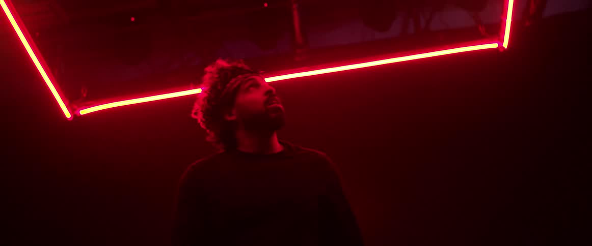 A man looks up at neon lights above him