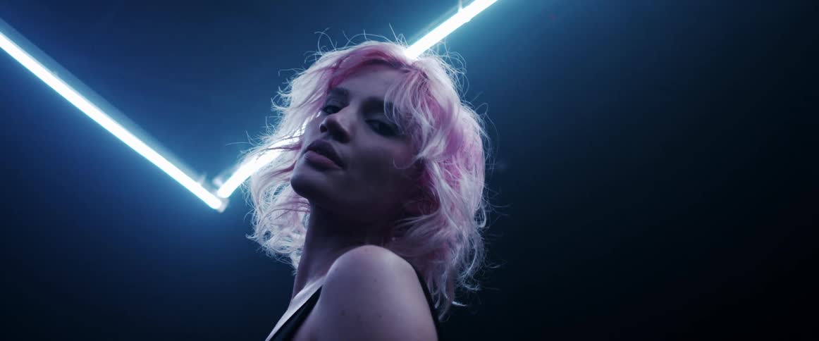 Young woman with pink hair looking at the camera on a dark room under blue neon lights