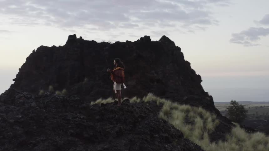 Man wearing traditional native attire looking at the horizon on a mountain top at sunset