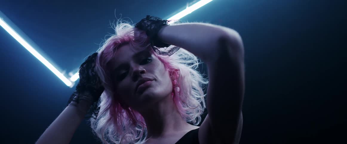 A model standing under neon lights rubs her hands on her head