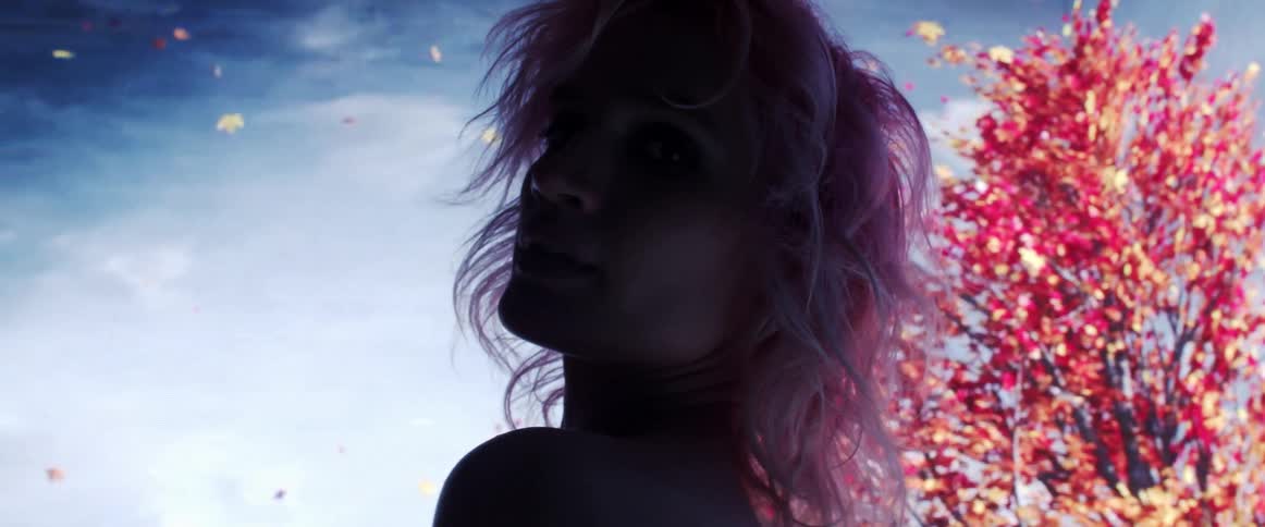 The silhouette of a woman is illuminated by a large screen displaying trees behind her