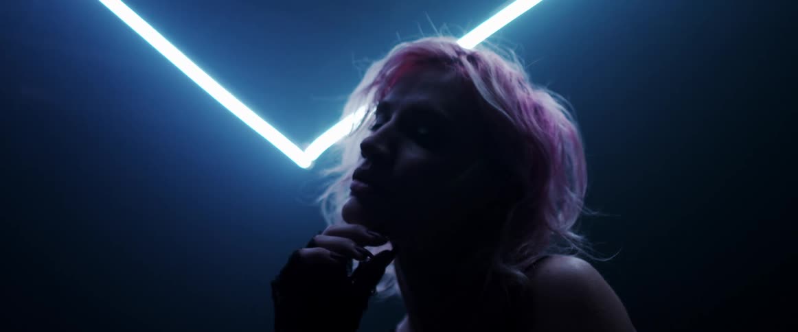 The silhouette of a woman with short blond hair posing for the camera is illuminated by neon lights