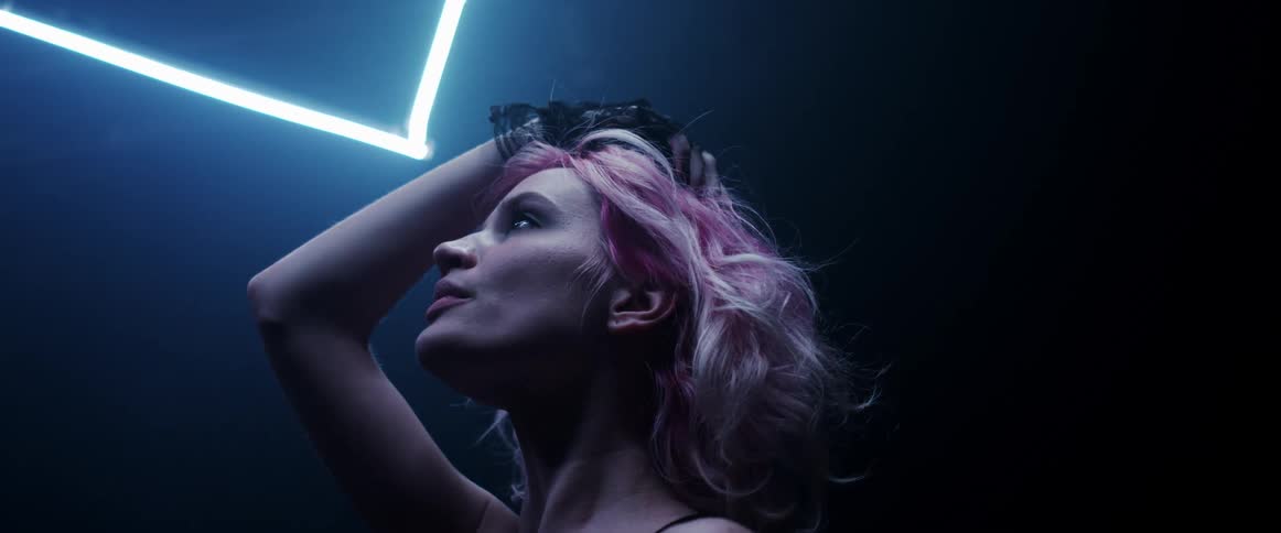 Young woman with pink hair standing on a dark room under blue neon lights