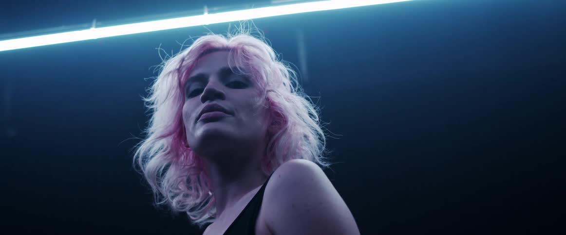A woman with pink tinted hair poses looking down with a glowing light above