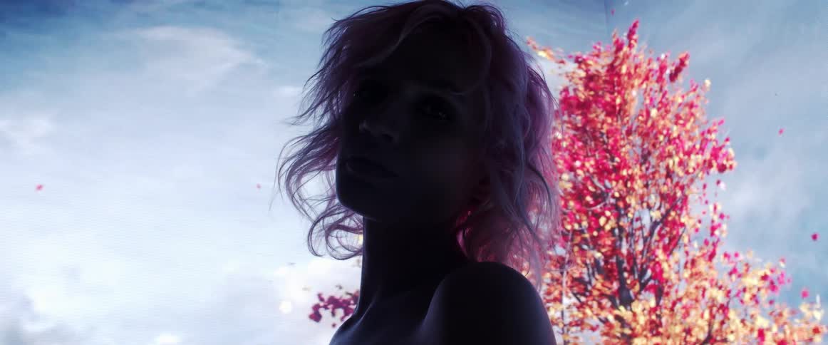 The silhouette of a woman with short blonde hair is illuminated by a large digital screen displaying digital images of trees