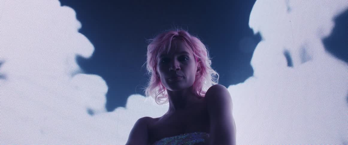 A woman standing and staring on a stage with a screen behind her