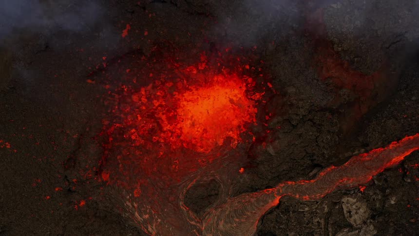 Erupting volcano spews molten hot lava into the air and oozes a river of hot lava glowing in the darkness