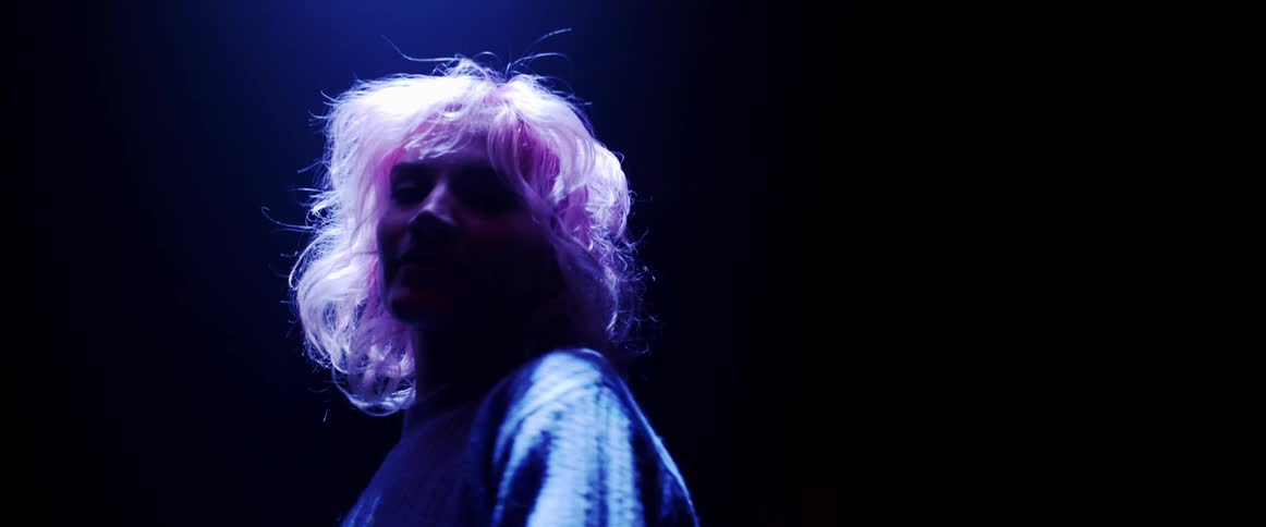 Young woman with pink hair looking at the camera dancing on a dark room