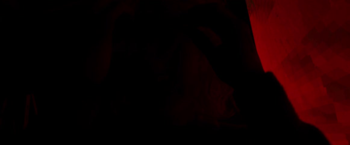 The silhouette of a woman with blond hair is illuminated by a large screen behind her