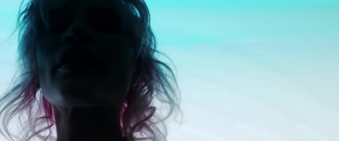Young woman with pink hair looking at the camera on a dark room in front of a digital display