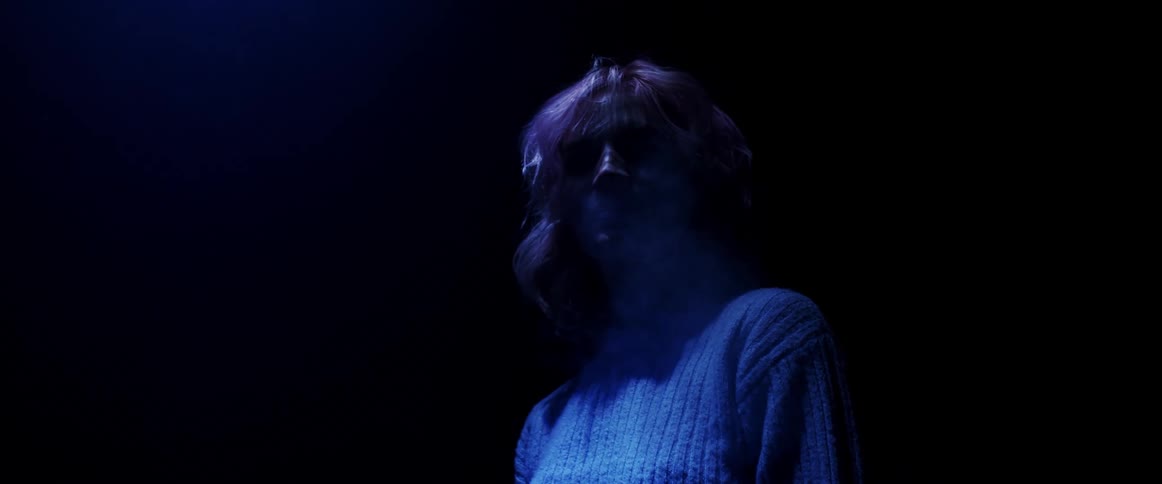 Young woman with pink hair looking at the camera with water vapour coming out of her nose on a dark room under blue neon lights