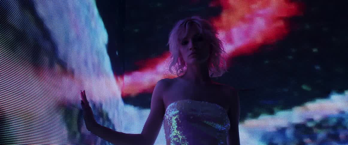 A model turns around and poses as she stands in front of a large screen showing digital graphics