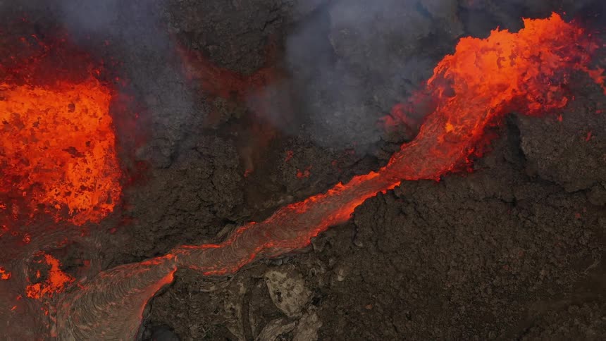 Erupting volcano spews molten hot lava and oozes a river of hot lava