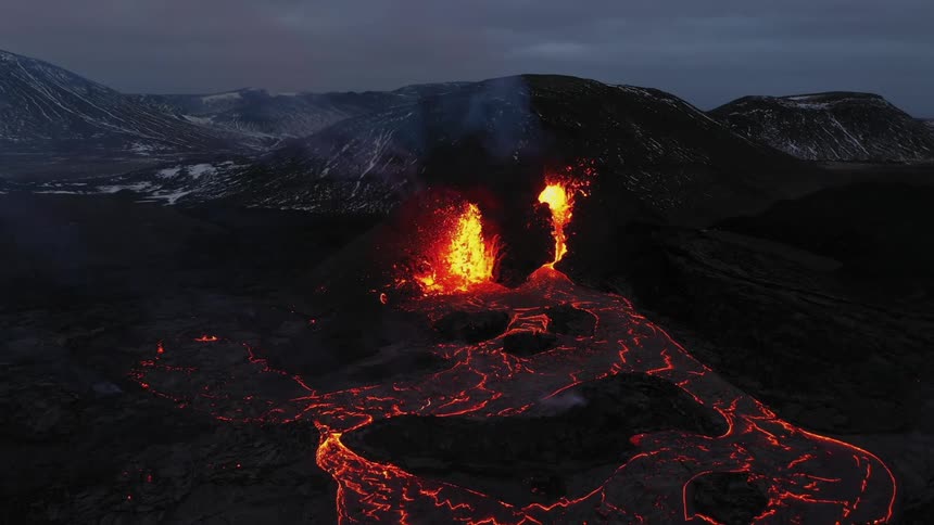 Erupting volcano spews molten hot lava and oozes a river of hot lava