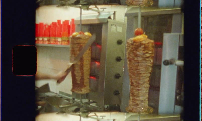 A cook cuts chicken from a vertical rotisserie