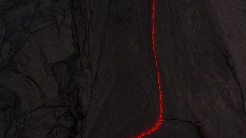 Aerial view of a stream of red hot lava flowing on a mountain slope